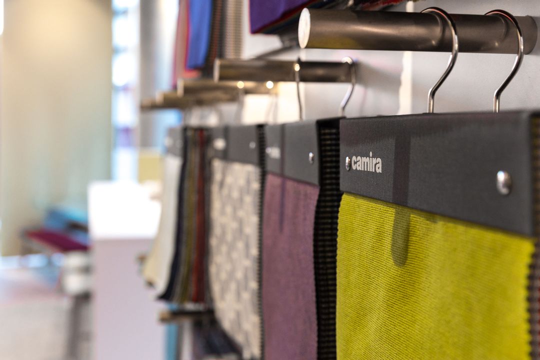 Close up of several of Camira's fabric swatches
                        hanging
                        from a bespoke made wall unit